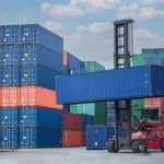 A forklift carrying a shipping container.
